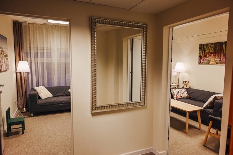 Zdjęcie z przedpokoju. Po prawej stronie widać pokój przesuchań, po lewej poczekalnię. Na ścianie pomiedzy tymi pokojami jest zawieszone lustro w srebrnej ramie. 